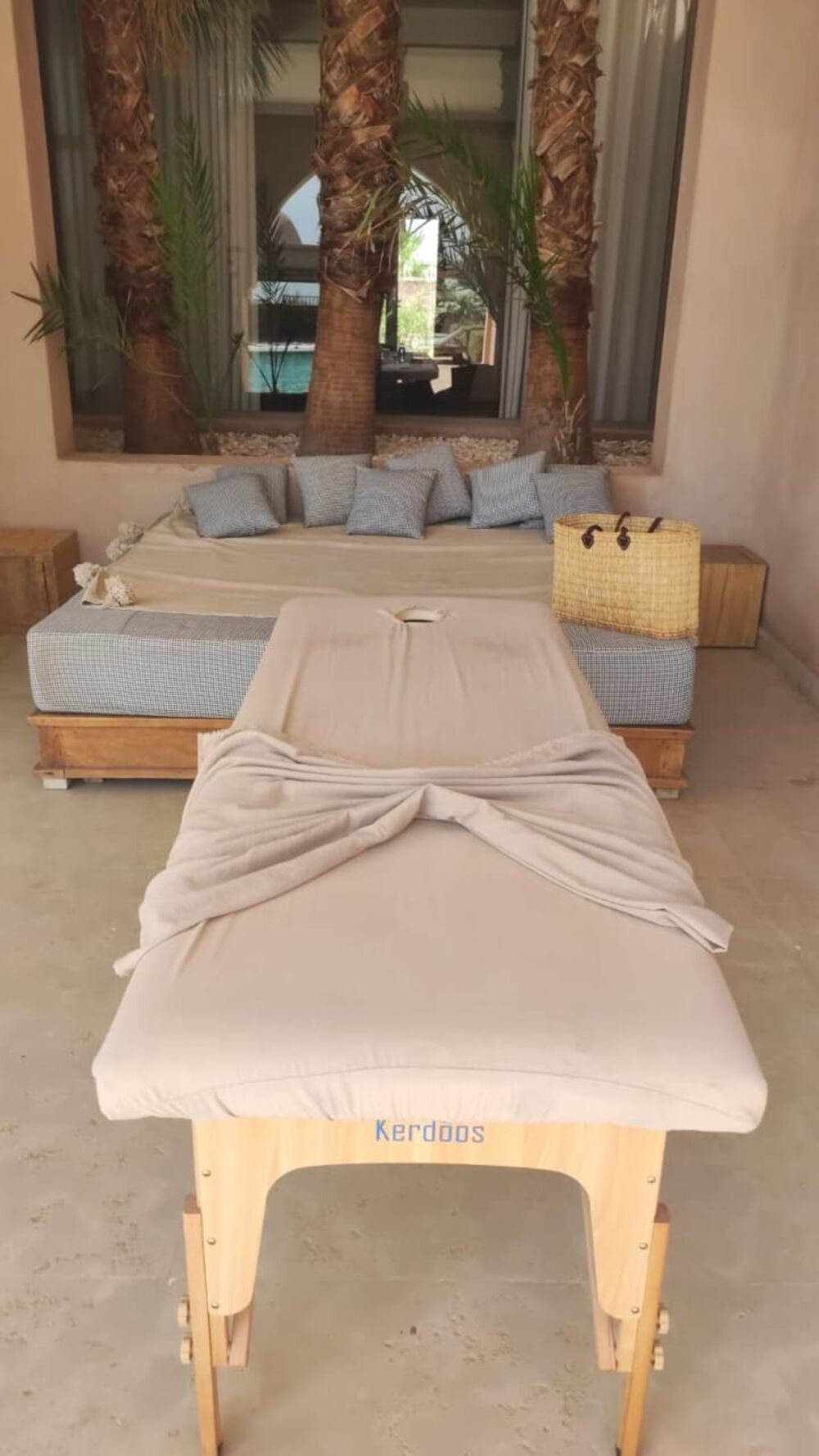Table de massage installée dans un salon extérieur ombragé entouré de palmiers, à Marrakech